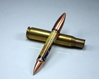 May include: A copper and brass pen with a design of the Declaration of Independence and the words "We the People" on the barrel. The pen is resting on a spent bullet casing.