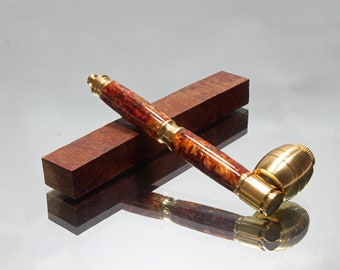 May include: A wooden pipe with a brass bowl and a red and gold marbled design. The pipe is resting on a wooden block.