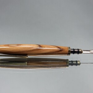 May include: A wooden thread cutter with a brass tip and a black and silver metal mechanism. The cutter is lying on a reflective surface.