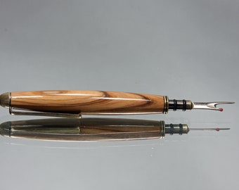 May include: A wooden thread cutter with a brass tip and a black and silver metal mechanism. The cutter is lying on a reflective surface.