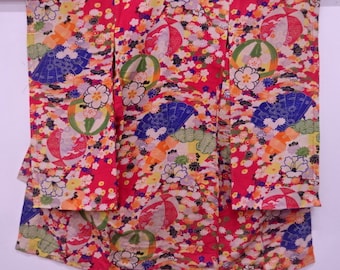 Pode incluir: Um quimono vermelho com um padrão floral colorido. O padrão inclui leques, flores e formas geométricas. O quimono é feito de seda e tem um design japonês tradicional.