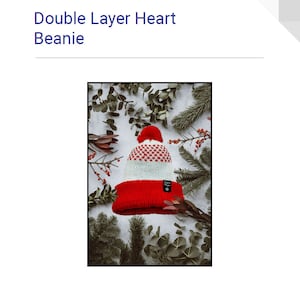 May include: A red and white double layer beanie with a white pom pom on top. The beanie has a small black label with the text "Dyson's Designs" on the side. The beanie is photographed on a white background with green foliage.