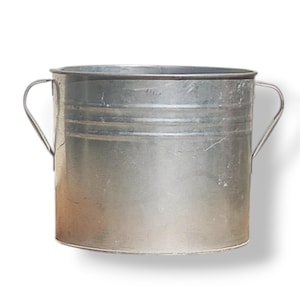 Op de afbeelding: Een gegalvaniseerde metalen emmer in zilverkleur met twee gebogen handvatten. De emmer heeft een cilindrische vorm met horizontale banden rond de body. Het metaal heeft een licht verweerde uitstraling.