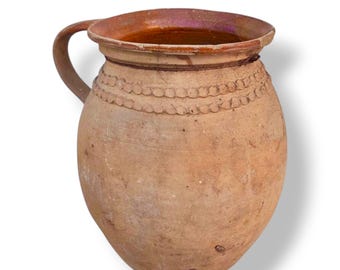 May include: A rustic, earthenware pitcher with a handle. The pitcher has a wide, slightly flared rim and a rounded body. A decorative band of small, raised circles encircles the neck. The color is a warm, earthy brown with variations in tone.