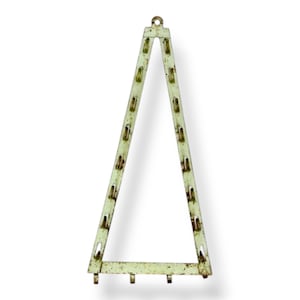 May include: A vintage, triangular metal display rack with a pale green finish and rust spots. The rack has multiple slots for holding items and a loop at the top for hanging. The base has three small feet.