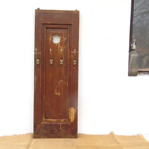 May include: A rustic wooden coat rack with four metal hooks. The rack is painted brown and has a distressed finish. It is mounted on a white wall.