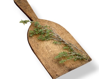 May include: A weathered, rectangular wooden cutting board with a tapered handle and a small loop of twine attached to the end. The surface of the wood shows signs of wear and texture. A sprig of fresh green thyme rests across the board.