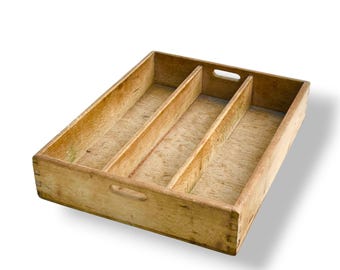 May include: A rectangular wooden cutlery tray with four compartments. The tray is made of light-colored wood and has a handle on each end. The dividers are vertical, creating separate spaces for utensils. The wood grain is visible.