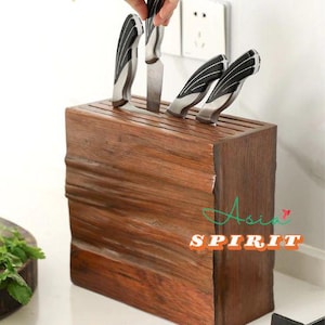 Könnte beinhalten: Ein Messerblock aus Holz mit mehreren Messern. Die Messer haben silberne Klingen und schwarz-silberne Griffe. Der Block ist dunkelbraun und hat eine strukturierte Oberfläche. Der Text "Asia Spirit" ist sichtbar.