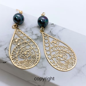 May include: Gold earrings with a black pearl and a delicate, intricate design featuring a flower and wave pattern.