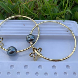 May include: Two gold bangle bracelets with a flower design and black pearl accents.