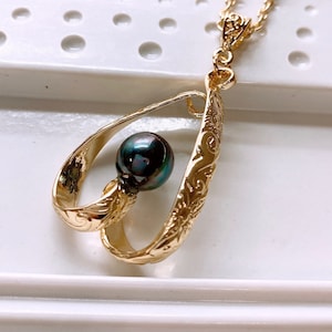 May include: A gold necklace with a black pearl pendant. The pendant is a delicate, open heart design with intricate floral details.