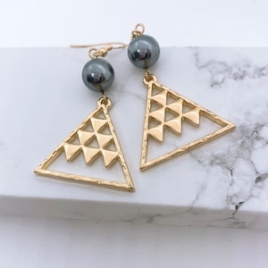 May include: Gold triangle earrings with a geometric pattern and a black pearl dangle.