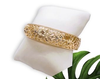 May include: A gold filigree bangle bracelet with a floral design. The bracelet is displayed on a white pillow.