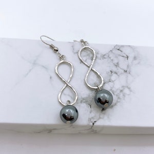 May include: Silver infinity symbol earrings with black pearl accents.