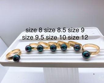 May include: Seven gold rings with black pearl accents. The rings are displayed on a white surface with the text "size 8 size 8.5 size 9 size 9.5 size 10 size 12".