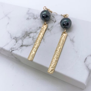 May include: A pair of gold earrings with a black pearl dangle. The gold is engraved with a floral pattern.