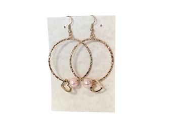 May include: A pair of gold hoop earrings with a textured finish. Each earring has a small heart charm with a pink pearl hanging from it.