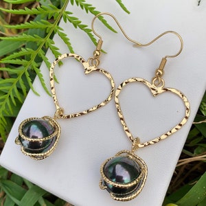 May include: Gold heart shaped earrings with a black pearl dangling from each heart.