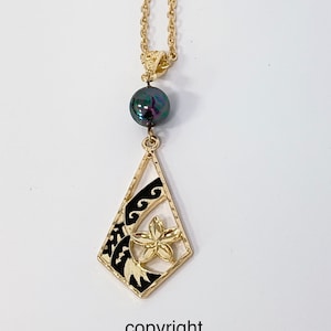 May include: A gold necklace with a black and gold pendant featuring a flower and wave design. The pendant is attached to a black pearl.
