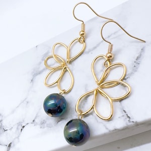 May include: Gold dangle earrings with a black pearl drop. The earrings feature a delicate, floral design.