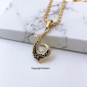 May include: Gold chain necklace with a black and gold pendant shaped like a traditional Hawaiian fish hook. The pendant has intricate details and a rope chain.