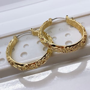 May include: A pair of gold hoop earrings with a detailed floral design. The earrings are made of metal and have a polished finish.