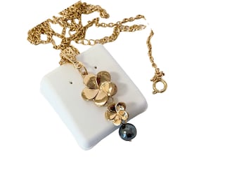 May include: A gold chain necklace with a pendant featuring two gold flower charms and a black pearl.