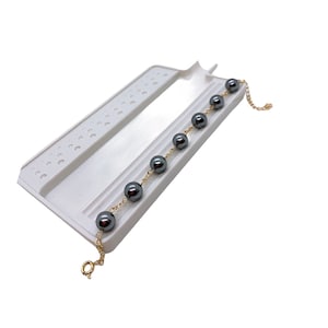 May include: A white plastic beading tray with a gold chain and black beads. The chain is threaded through the beads and is laying on the tray.
