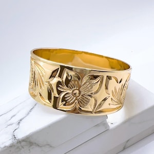 K&ouml;nnte beinhalten: Ein breiter goldfarbener Ring mit einem floralen Design. Der Ring ist aus Metall und hat eine glatte, polierte Oberfl&auml;che.
