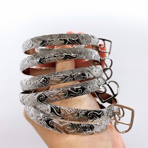 May include: Five silver bracelets with a floral design. The bracelets are stacked on top of each other and have a heart-shaped clasp.