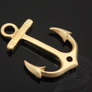 Könnte beinhalten: Ein goldfarbener Anker-Anhänger aus Metall mit einer Schlaufe oben. Der Anker ist ein beliebtes nautisches Symbol.