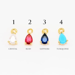 Peut inclure: Quatre breloques en forme de goutte d'or avec des pierres précieuses de différentes couleurs. Les breloques sont numérotées de 1 à 4. Les pierres précieuses sont le cristal, le rubis, le saphir et la turquoise.