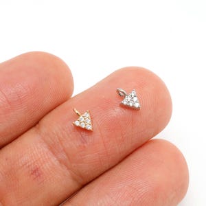May include: Two small, triangle-shaped pendants. One is gold-toned and set with clear gemstones, the other is silver-toned and also set with clear gemstones. Both pendants are displayed on a light background.