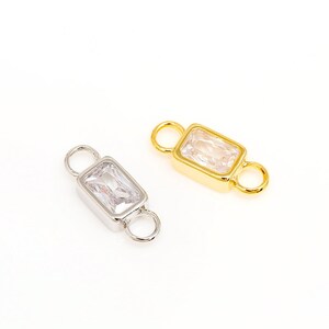May include: Two gold and silver connector charms with clear rectangular stones. The charms have two loops for attaching to jewellery.
