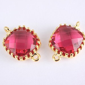 Puede incluir: Dos conectores metálicos dorados con un cristal rosa facetado de forma cuadrada en el centro. Cada conector tiene un bucle a cada lado.