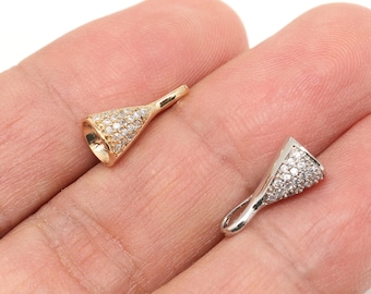 May include: Two small, cone-shaped jewellery findings. One is gold-toned and the other is silver-toned. Both are encrusted with small, clear gemstones. The findings are held in a person's hand.