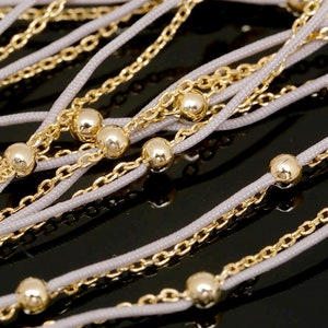 Può includere: Una collana multifilo con catena e perline dorate e un cordoncino grigio chiaro.
