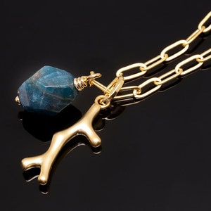 K&ouml;nnte beinhalten: Eine goldene Kettenkette mit einem blauen Edelstein-Anh&auml;nger und einem goldenen Ast-Anh&auml;nger.