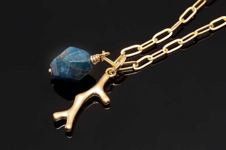 K&ouml;nnte beinhalten: Eine goldene Kettenkette mit einem blauen Edelstein-Anh&auml;nger und einem goldenen Ast-Anh&auml;nger.