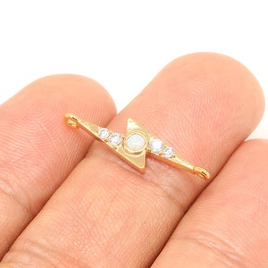 Op de afbeelding: Goudkleurige bliksemvormige bedel met heldere en witte opaalachtige stenen. De bedel heeft aan elk uiteinde een lus om aan sieraden te bevestigen.