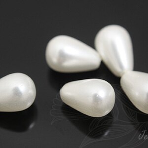 May include: Several off-white, teardrop-shaped beads with a pearlescent sheen are arranged against a dark background. The beads have a smooth, rounded form, suggesting they are for jewelry making or crafts.
