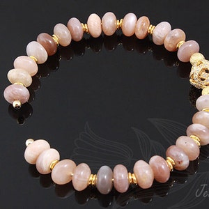 May include: A gold bracelet with a sunstone bead design. The bracelet has a gold clasp with a decorative design.