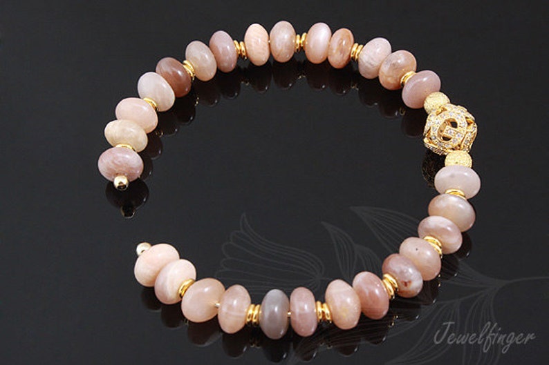 May include: A gold bracelet with a sunstone bead design. The bracelet has a gold clasp with a decorative design.