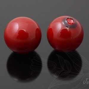 May include: Two red glass beads, one with a small black spot on the top.