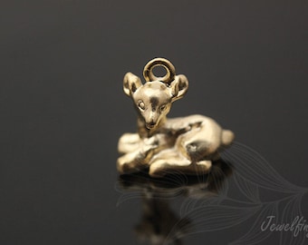 May include: A gold-colored metal charm in the shape of a sitting deer. The deer has a small loop at the top of its head for attaching to a necklace or bracelet.