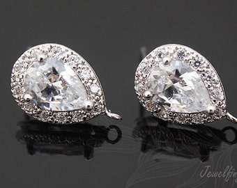 May include: A pair of silver teardrop-shaped earring findings with clear cubic zirconia stones. The stones are set in a halo setting and the findings have a loop for attaching a dangle.
