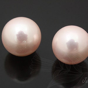 May include: Two round, pale pink pearls with a smooth, glossy finish. The pearls are set against a black background.