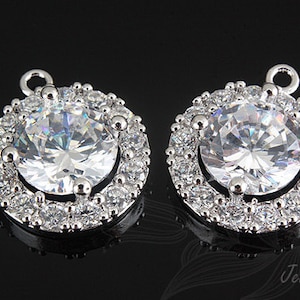 Puede incluir: Un par de pendientes de plata con una gran piedra redonda de circonita cúbica transparente rodeada por un halo de piedras de circonita cúbica más pequeñas.