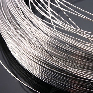 May include: A close-up of a spool of silver-colored wire. The wire is tightly wound and has a smooth, shiny finish.